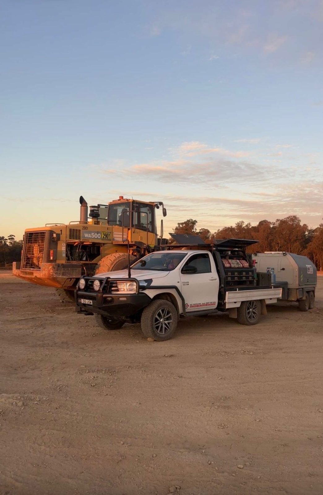 JSM service ute and trailer beside a Komatsu WA500 loader at sunset